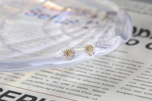 Macro shot of silver daisy stud earrings with gold center on vintage paper background