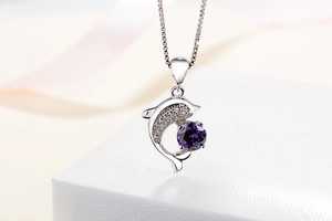 Detail of dolphin pendant necklace with purple zircon and silver box chain on satin
