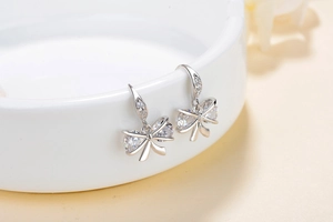 Elegant S925 silver bow earrings with sparkling cubic zirconia on a white ceramic display
