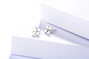 Gros plan de boucles d'oreilles trèfle en argent S925 sur support géométrique blanc