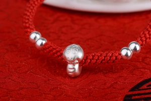 Macro view of handmade red braided cord bracelet with silver beads and cartoon horse charm