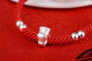 Macro shot of a matte silver ox charm with polished beads on a woven red cord bracelet