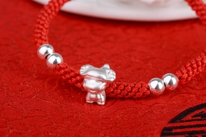 Close-up of hand-woven red rope bracelet with a 3D silver zodiac charm and beads