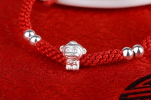 Macro shot of S999 silver monkey pendant on hand-woven red rope bracelet for luck