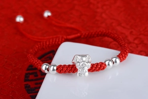 Macro view of hand-woven red cord bracelet with S999 silver zodiac dog and silver beads