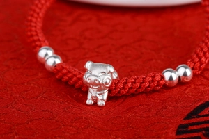 Macro view of silver zodiac pig pendant on handmade braided red cord bracelet