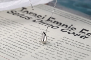 Détail d'un pendentif goutte en argent poli sur une fine chaîne sur un journal