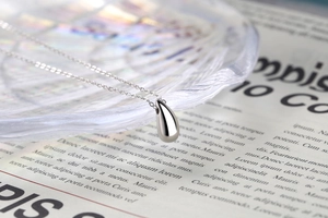 Macro d'un pendentif goutte d'eau poli en argent sterling S925 minimaliste sur chaîne fine