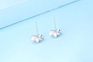Close-up of S925 sterling silver four-leaf clover stud earrings on light blue surface