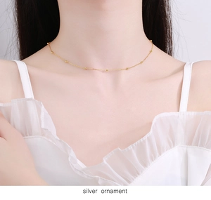 Detail of a thin gold beaded choker necklace worn by a model in a white ruffled outfit