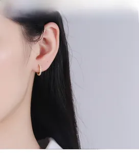 Close-up of golden S925 silver hoop earrings with white crystals on a model's ear