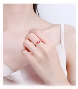 Detail of heart-cut ruby ring with rose gold band and sparkling accents on finger