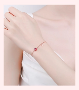Detailed macro view of a rose gold bracelet featuring a red heart and crystal charm