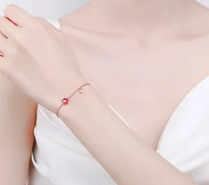 Close-up of rose gold bracelet featuring a red heart pendant and zircon on wrist