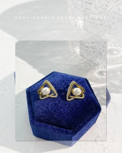Dettaglio orecchini a triangolo con perle placcati in oro su portagioie in velluto blu