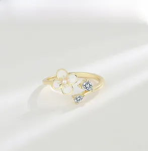Macro view of golden flower ring with white enamel petals, tiny pearl and heart zircon