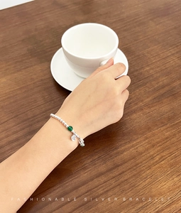 Detail of S925 silver beaded bracelet with green bead and Fu character charm on hand