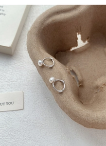 Détail de boucles d'oreilles créoles en argent S925 avec perles sur fond texturé rustique
