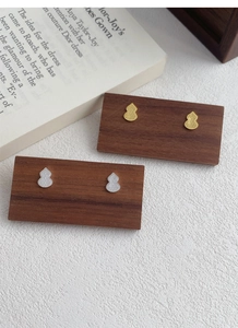 Macro shot of silver and gold gourd stud earrings on a wooden display card