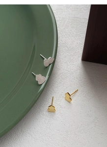 Macro detail of gold and silver Wulu stud earrings with textured finish on ceramic tray