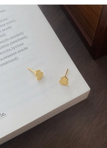 Detailed view of gold gourd earrings with matte texture and diamond pattern on white book