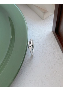 Detail of S925 silver fish ring engraved with Smile text on a ceramic plate