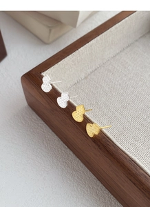 Close-up of heart-shaped S999 silver earrings with hammered texture on wooden tray