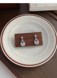 Detailed view of silver teardrop earrings with chalcedony and pavé stones on wood