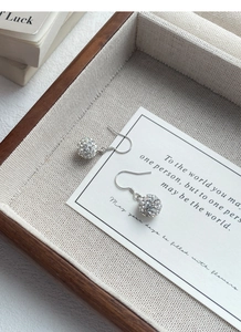 Detail of silver S925 drop earrings with pave crystal spheres on rustic linen tray