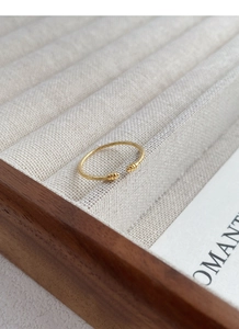 Close-up of minimalist gold twisted rope ring with bead ends on a beige linen jewelry tray