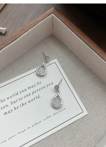 Macro shot of silver drop earrings with white chalcedony on a wooden display tray