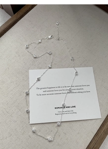 Detail of silver station necklace with round zircons on a wooden tray with linen fabric