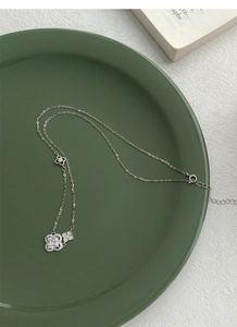Détail du collier trèfle en argent S925 avec diamant carré posé sur un plateau vert foncé