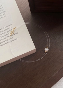 Close-up of a minimalist pearl on invisible nylon wire with a gold clasp on a book