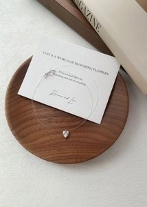 Detail of heart zircon pendant on invisible fishline chain displayed on a wooden tray
