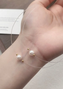Detail of a floating pearl necklace with a transparent line on a person's wrist