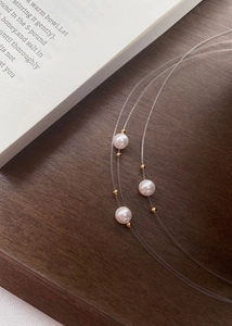 Macro shot of minimalist white pearl necklace with transparent fish line and gold bead details