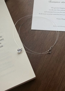 Macro detail of a heart-shaped zircon pendant on a transparent fishing line necklace