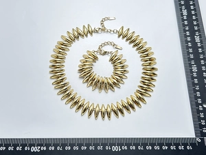 Detailansicht des goldenen Halsketten- und Armband-Sets im Bullet-Design auf weißem Ständer