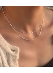 Detailopname van een gelaagde S925 zilveren Chopin-ketting op een witte gebreide trui
