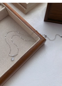Dettaglio della collana in argento S925 con nodo e zirconi lucidi su vassoio in legno