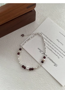 Detailed view of S925 silver bracelet with garnet beads and heart charm on white paper