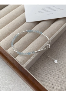 Dettaglio del ciondolo a cuore in argento S925 e perline blu su vassoio di lino