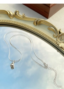 Macro detail of silver teardrop pendant necklace on vintage mirror with sky reflections