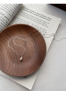 Macro detail of silver water drop necklace pendant with star engraving on wood