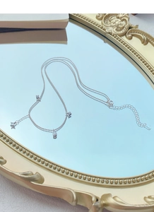 Détail macro du collier double en argent S925 avec pendentifs zircons sur un miroir