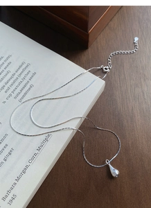 Detailed close-up of S925 sterling silver waterdrop pendant with small zircon on a book