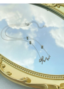 Detail of 925 silver necklace with diamond bow pendant and pearls on a mirror