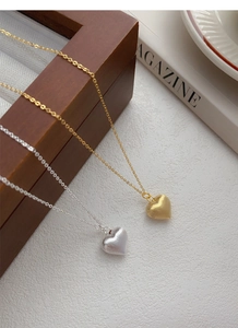 Detail of gold and silver heart necklaces with brushed metal finish on wood