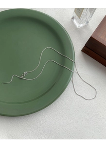 Detail view of S925 sterling silver thin chain necklace on dark green ceramic plate